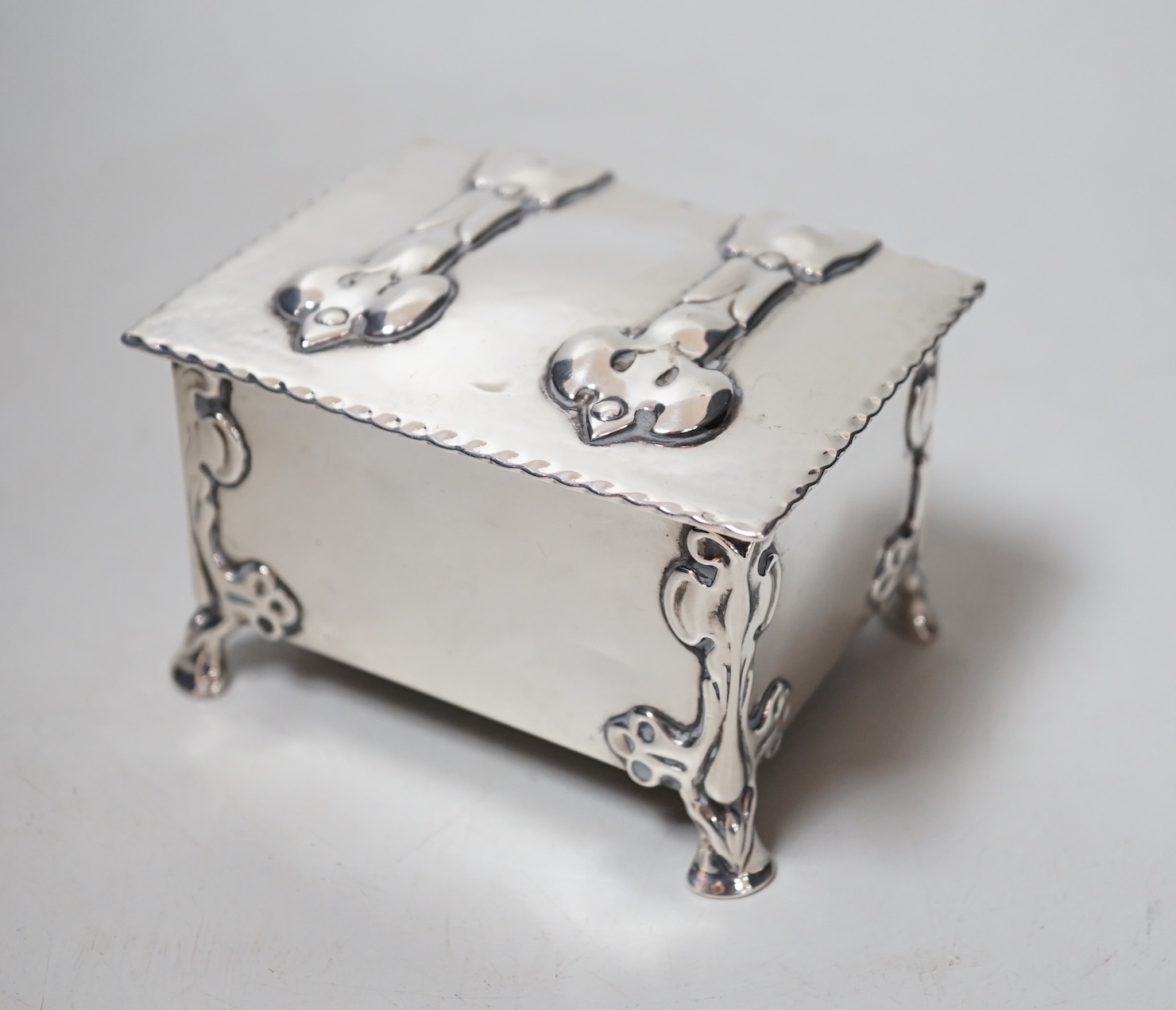 An Edwardian Arts & Crafts Kate Harris for William Hutton & Sons rectangular silver box, of lidded casket form, with relief cast foliate bracket feet, strap hinges and cedar lined interior, London, 1902, width 10.2cm, gr